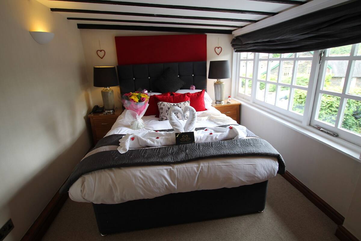 A neatly made bed with a red headboard, two bedside lamps, and a bouquet of flowers.