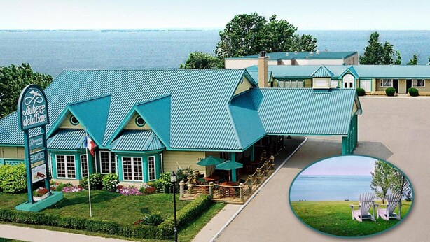 A coastal hotel with a prominent sign, outdoor seating, and a view of the sea. - Auberge de la Baie (Caraquet)
