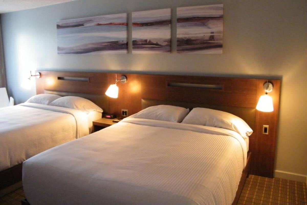 Een hotelkamer met twee bedden, een houten hoofdbord, bedlampjes en een kunstwerk aan de muur.