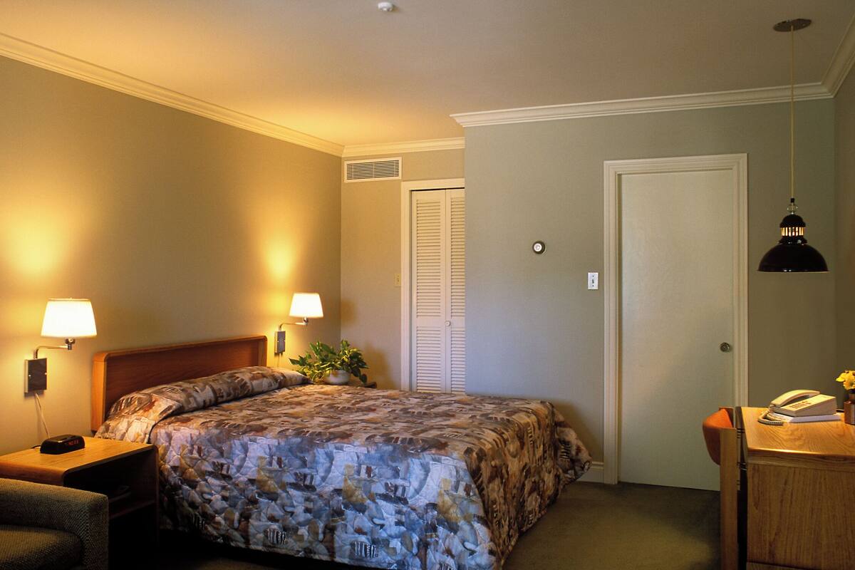 Een hotelkamer met een bed, nachtlampjes, een bureau met telefoon en een deur.