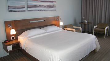 A hotel room with a large bed, two bedside lamps, a nightstand, a chair, a small table, and two abstract paintings on the wall.