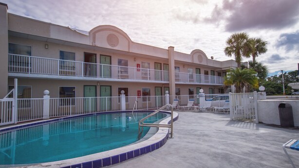 A hotel with a swimming pool, multiple balconies, and palm trees.