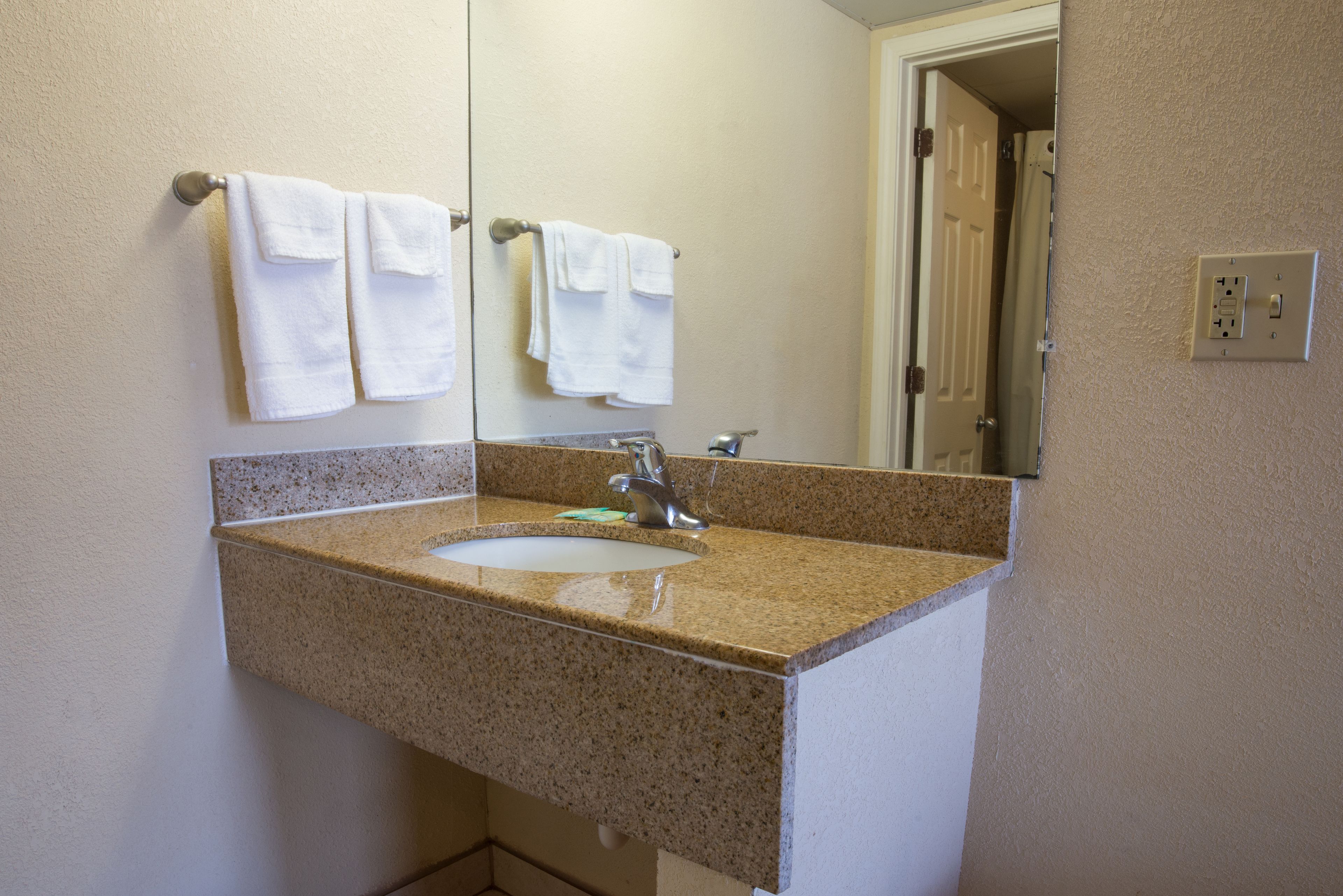 Une salle de bain avec un lavabo doté d’un plan de travail en granit, un miroir et deux serviettes blanches suspendues à un porte-serviettes.