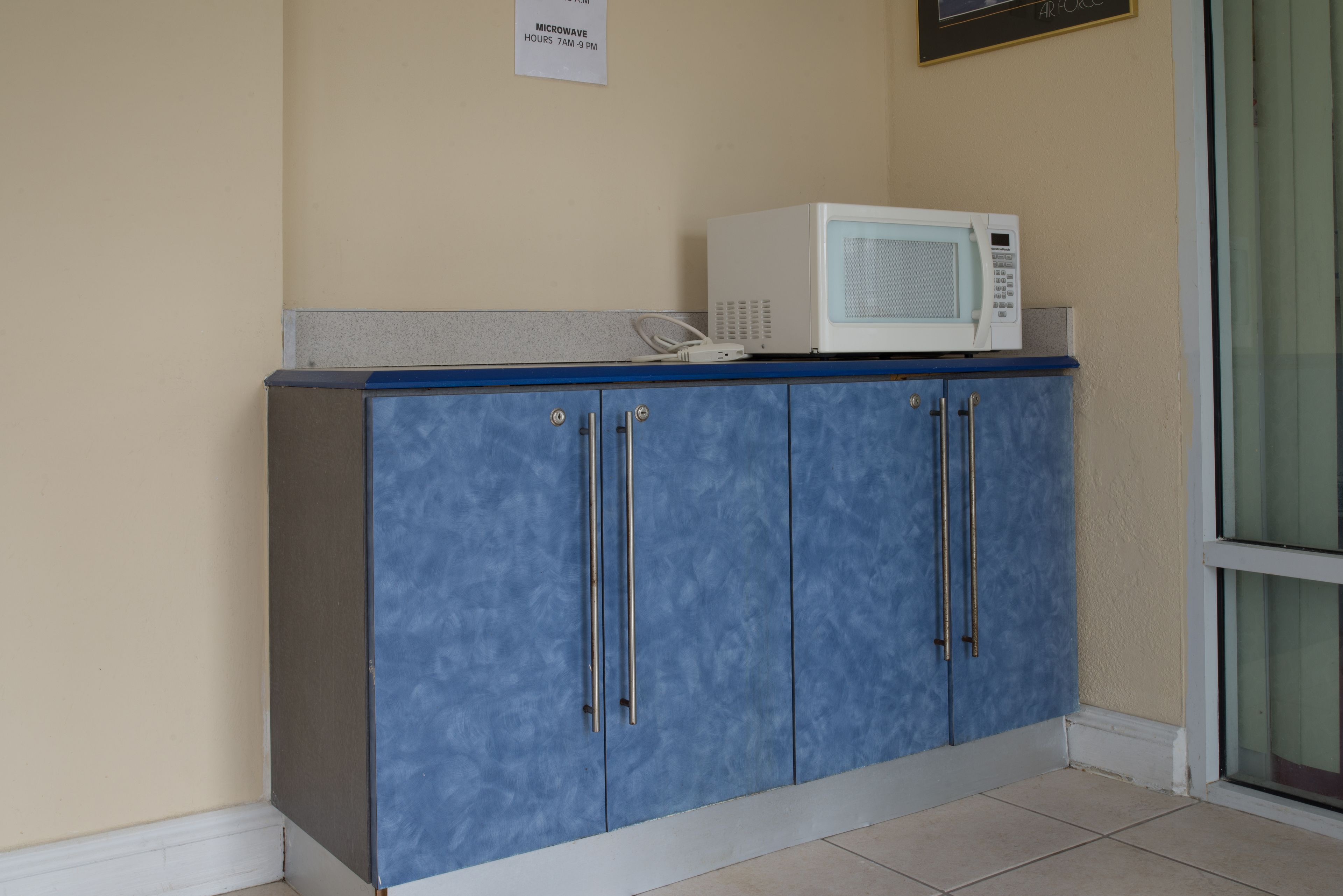 Un gabinete azul con un microondas encima, un cartel que indica el horario de uso del microondas y una puerta con un panel de vidrio.