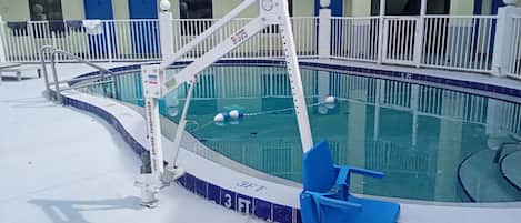 Zona de piscina con un elevador de piscina, una silla de piscina azul y un edificio con balcones al fondo.