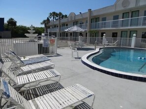 A pool area with lounge chairs and a building with balconies.