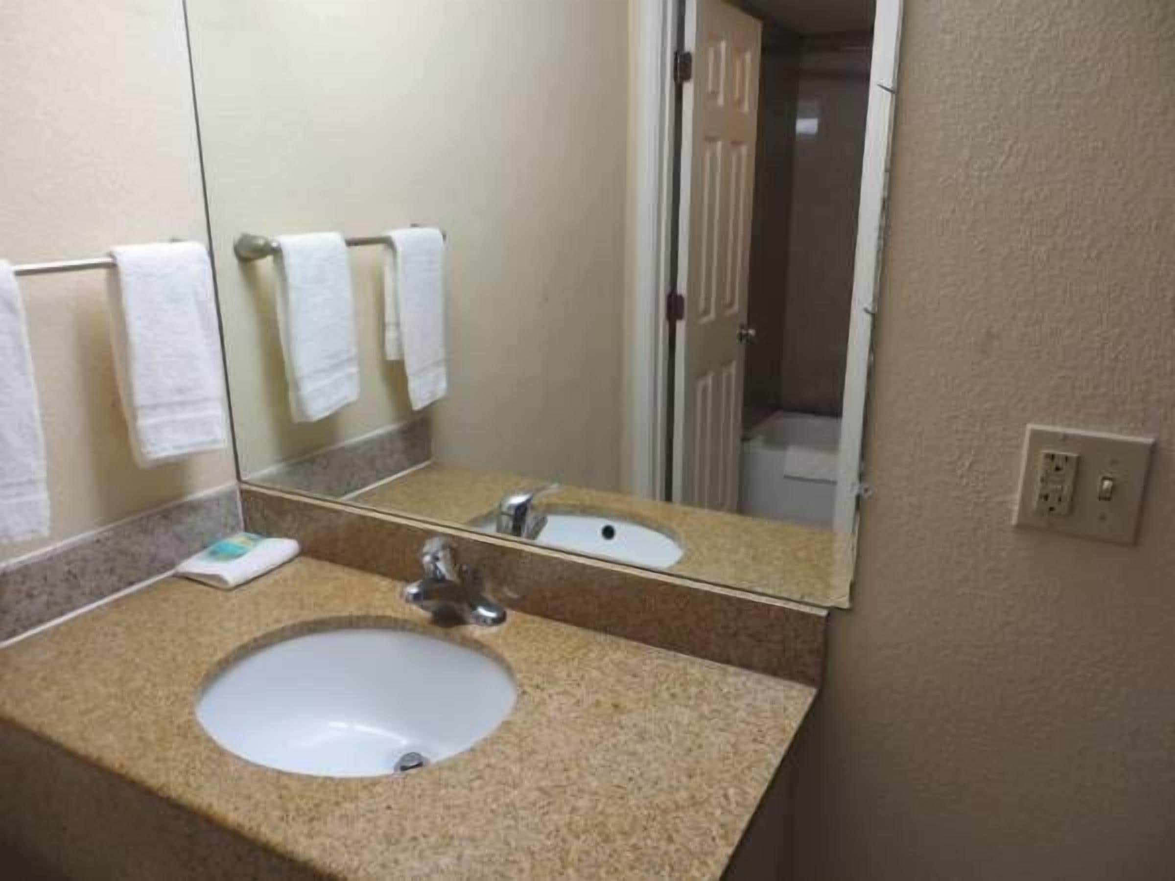 Un baño con lavamanos, espejo y toallero.