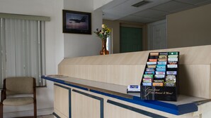 A reception desk with a blue counter, a framed picture on the wall, a vase with flowers, and a signboard with various advertisements.