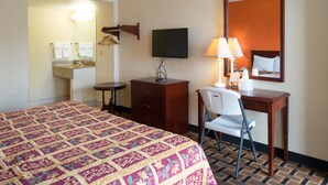 A hotel room with a large bed, a desk with a chair, a television, a desk lamp, and a mirror.