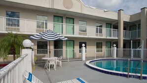A hotel with a pool area, including lounge chairs and umbrellas, and a two-story building with balconies.