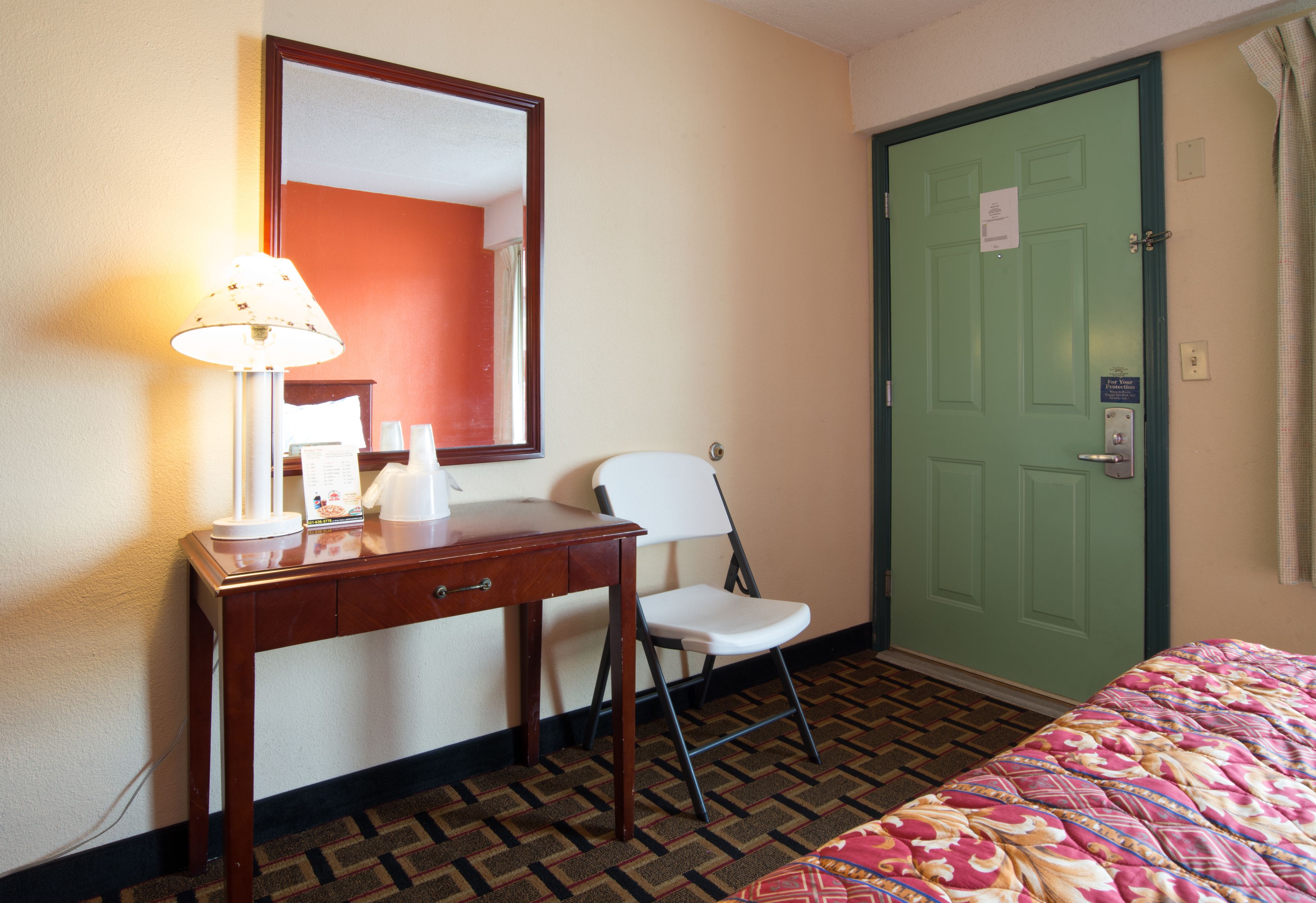A hotel room with a desk, chair, bed, and a green door.