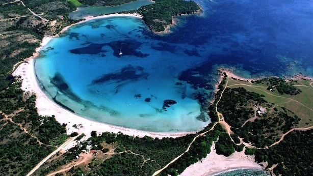 Vista aérea de una zona costera con una gran bahía, playas de arena y vegetación circundante.