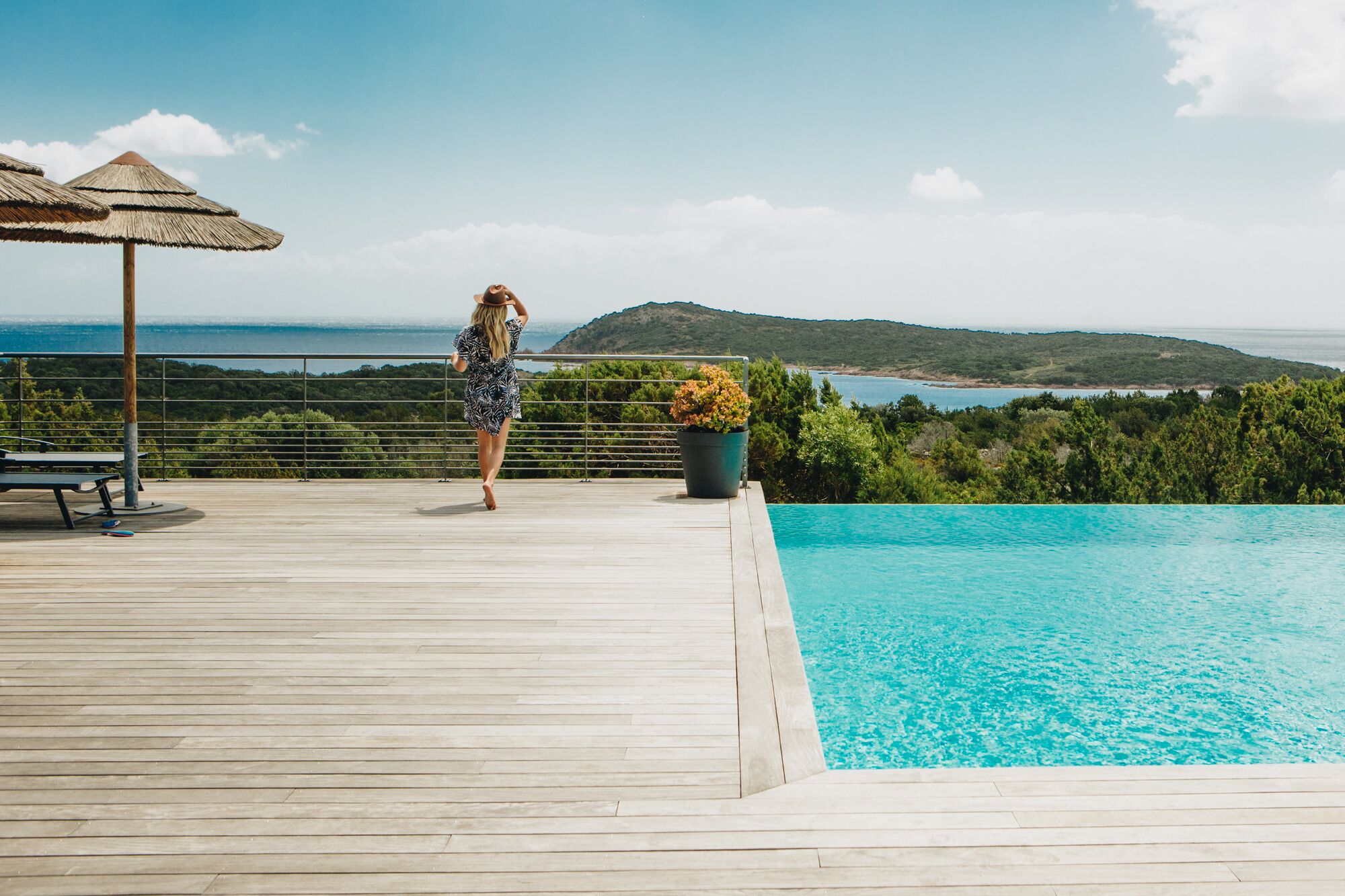 Une terrasse en bois avec une piscine, une plante en pot et une table.