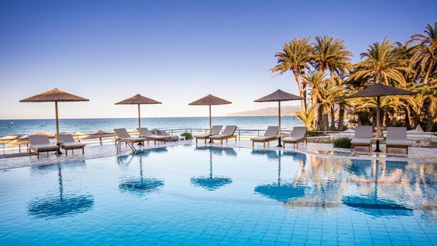 Zona junto a la piscina con sillones reclinables y sombrillas, con vista al mar.