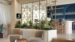 Un vestíbulo con mostrador de recepción, dos sillones estampados, una mesa de centro, una pared decorativa y una zona de bar con estanterías.