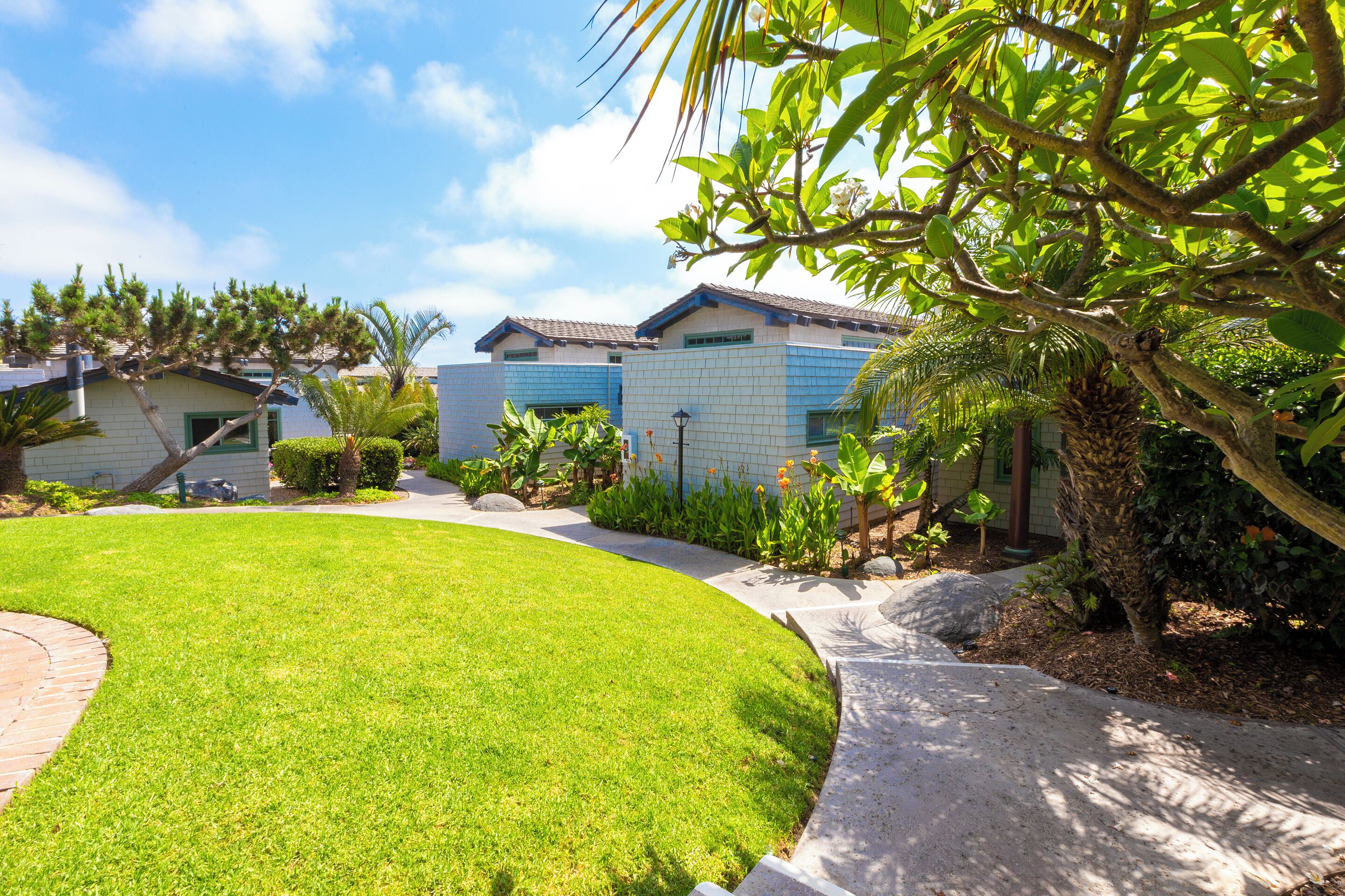 A residential area with a well-maintained lawn, a curved pathway, and houses with blue and white exteriors.