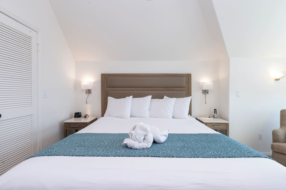 Habitación de hotel con una cama grande, dos mesitas de noche, una silla y una lámpara de pared.