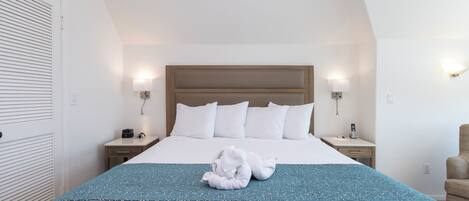 A hotel room with a large bed, two bedside tables, a nightstand, a chair, and a wall-mounted lamp.