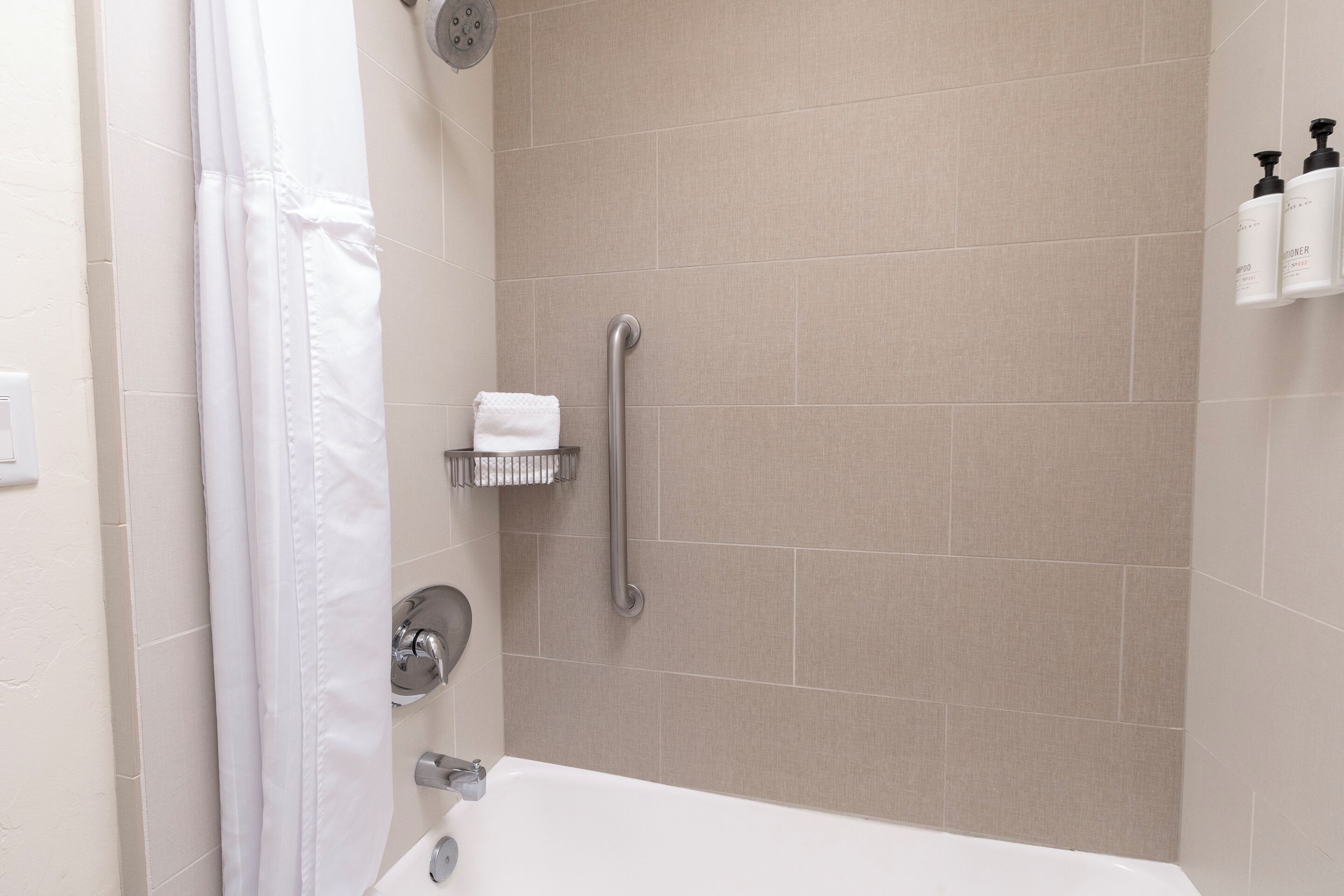 A modern bathroom with a bathtub, a shower with a grab bar, and a towel rack.