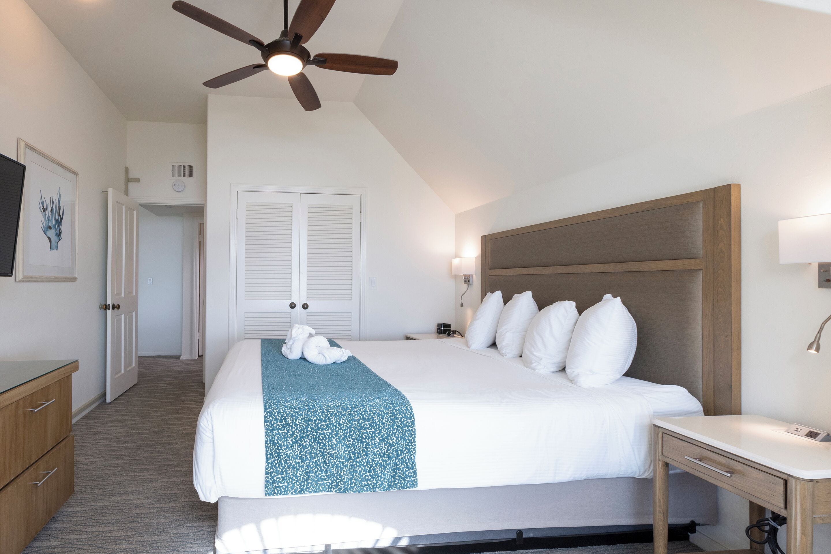 Ein Hotelzimmer mit einem großen Bett, einem Deckenventilator, einem Nachttisch und einem Schreibtisch.