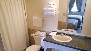 A bathroom with a toilet, sink, and a mirror. There are towels on the wall and a window with curtains. - Traveler's Choice Motel (Bay St Louis)