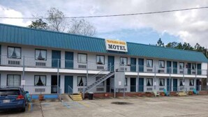 A motel with a blue roof, multiple balconies, and a parking lot. - Traveler's Choice Motel (Bay St Louis)