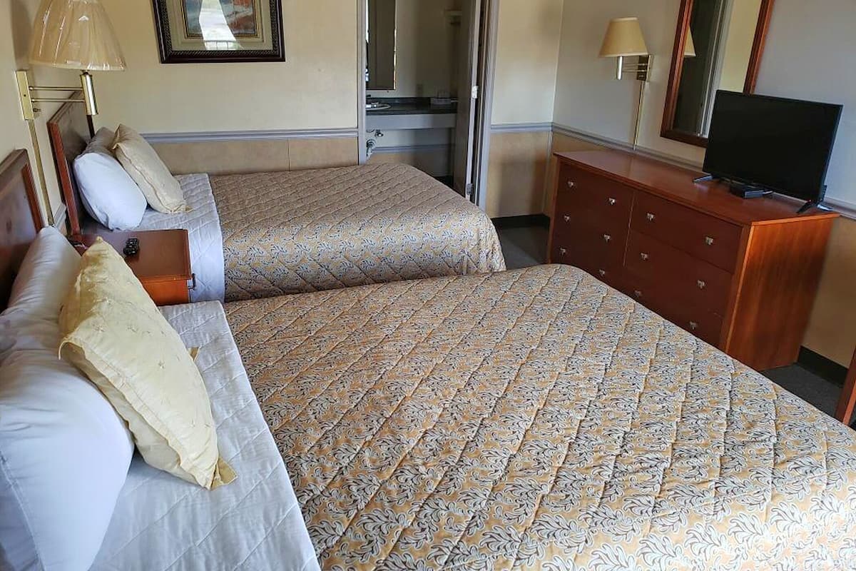A hotel room with two beds, a dresser, a television, and a mirror.