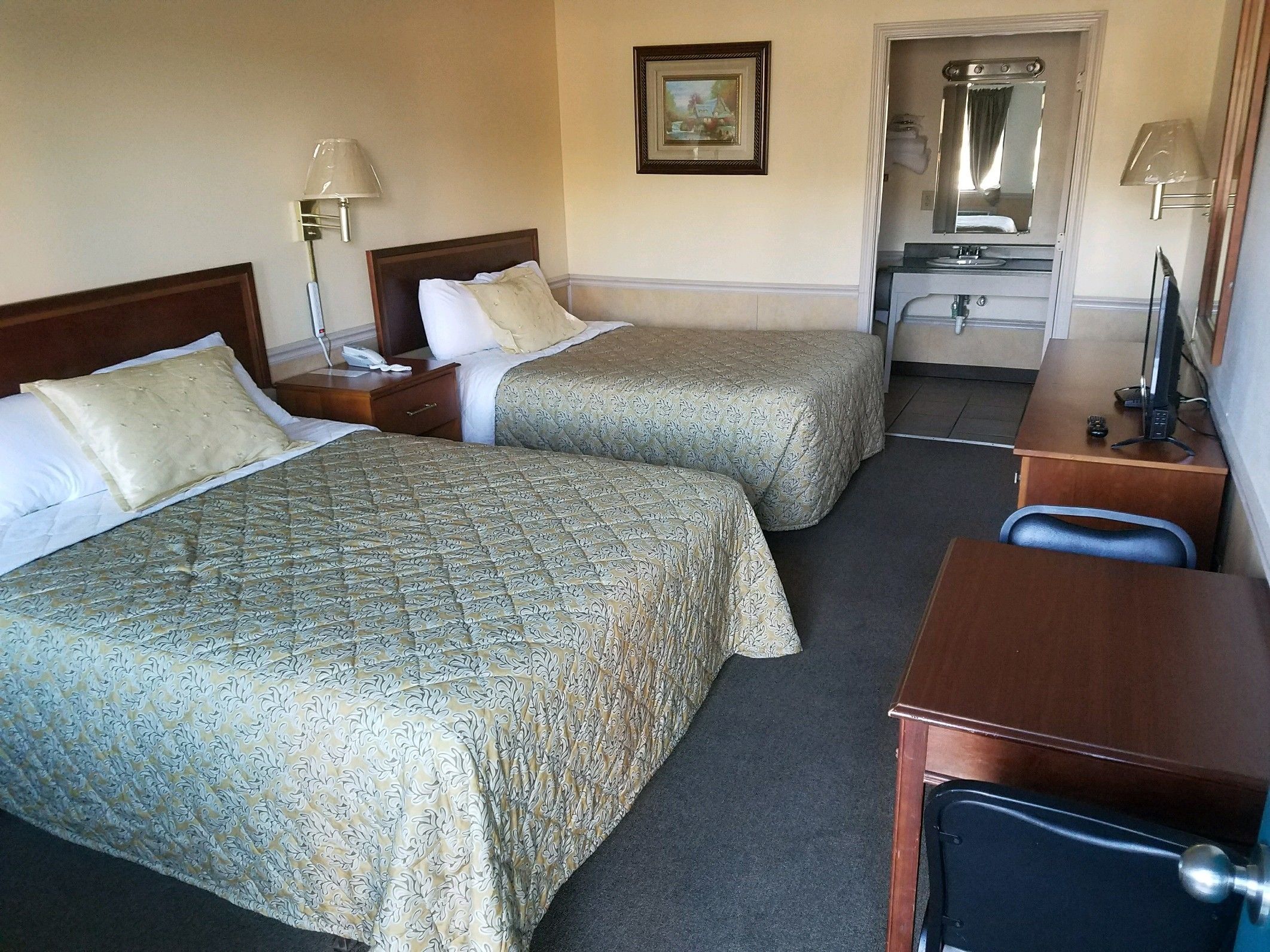 Une chambre d’hôtel avec deux lits, un bureau, une chaise, un miroir et une petite salle de bain.
