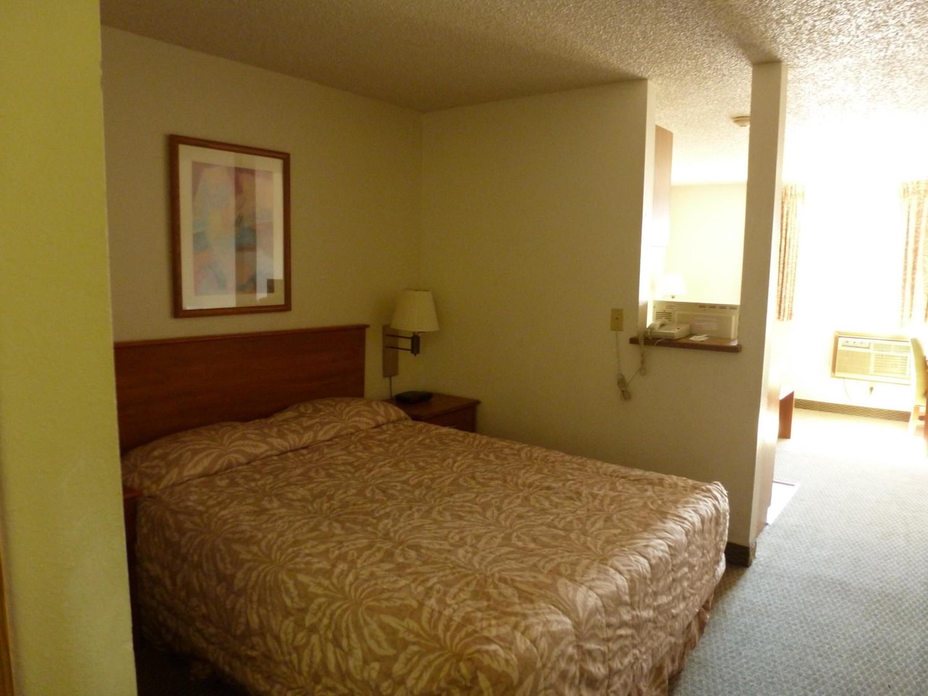 A hotel room with a large bed, a nightstand with a lamp, a framed picture on the wall, and a telephone on a shelf.