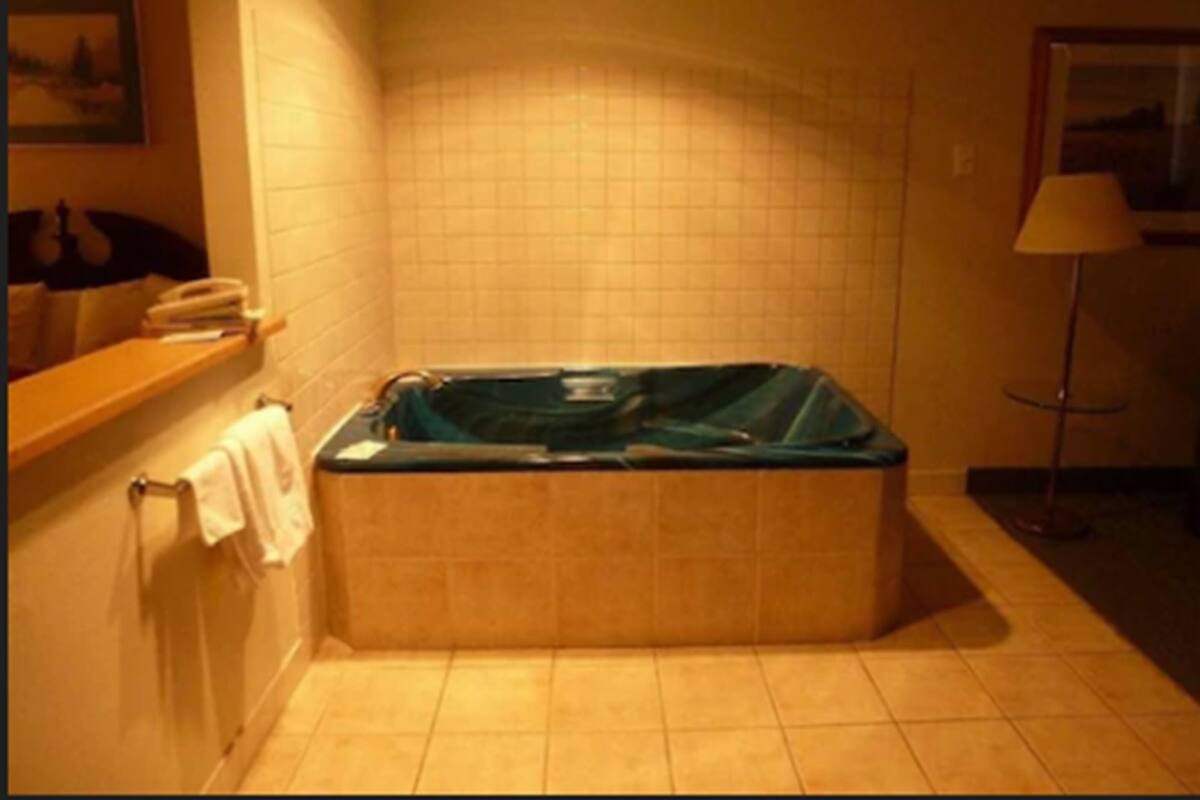 A bathroom with a bathtub, a towel rack, a shelf with books, and a lamp.