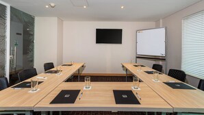 Un salón de conferencias con una larga mesa, sillas, una pizarra y una pantalla para proyector.