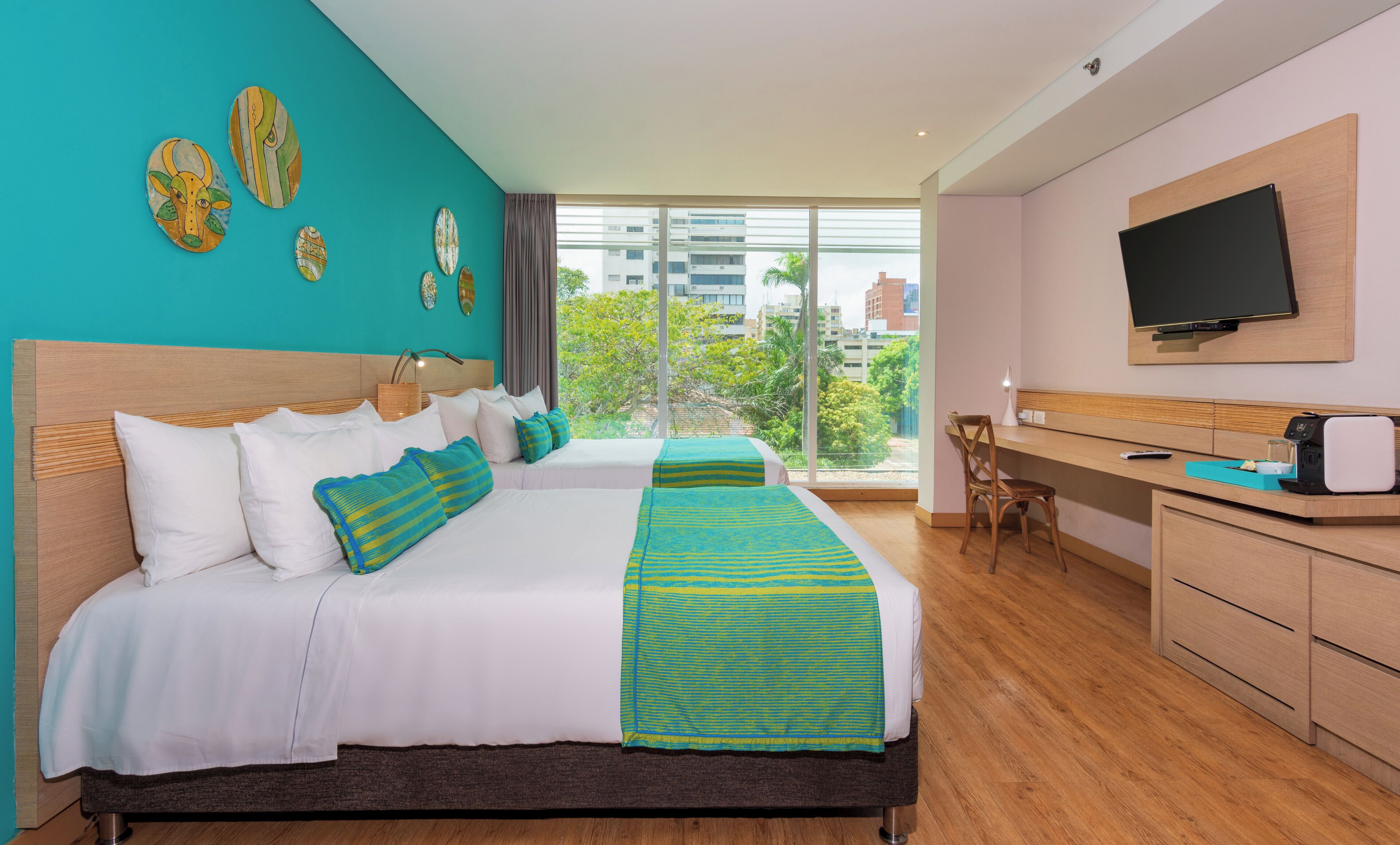 Habitación de hotel con cama, escritorio, silla, televisor y vista a la ciudad.