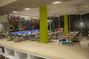 A modern restaurant with colorful graffiti art on the walls, green pillars, and a variety of seating options including booths and tables. - BH Barranquilla (Barranquilla)