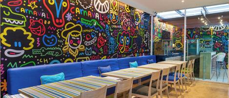 A vibrant restaurant interior with colorful murals, blue seating, and wooden tables.