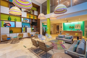 Un vestíbulo moderno con muebles de mimbre, lámparas colgantes de colores y un mostrador de recepción con una pared verde.