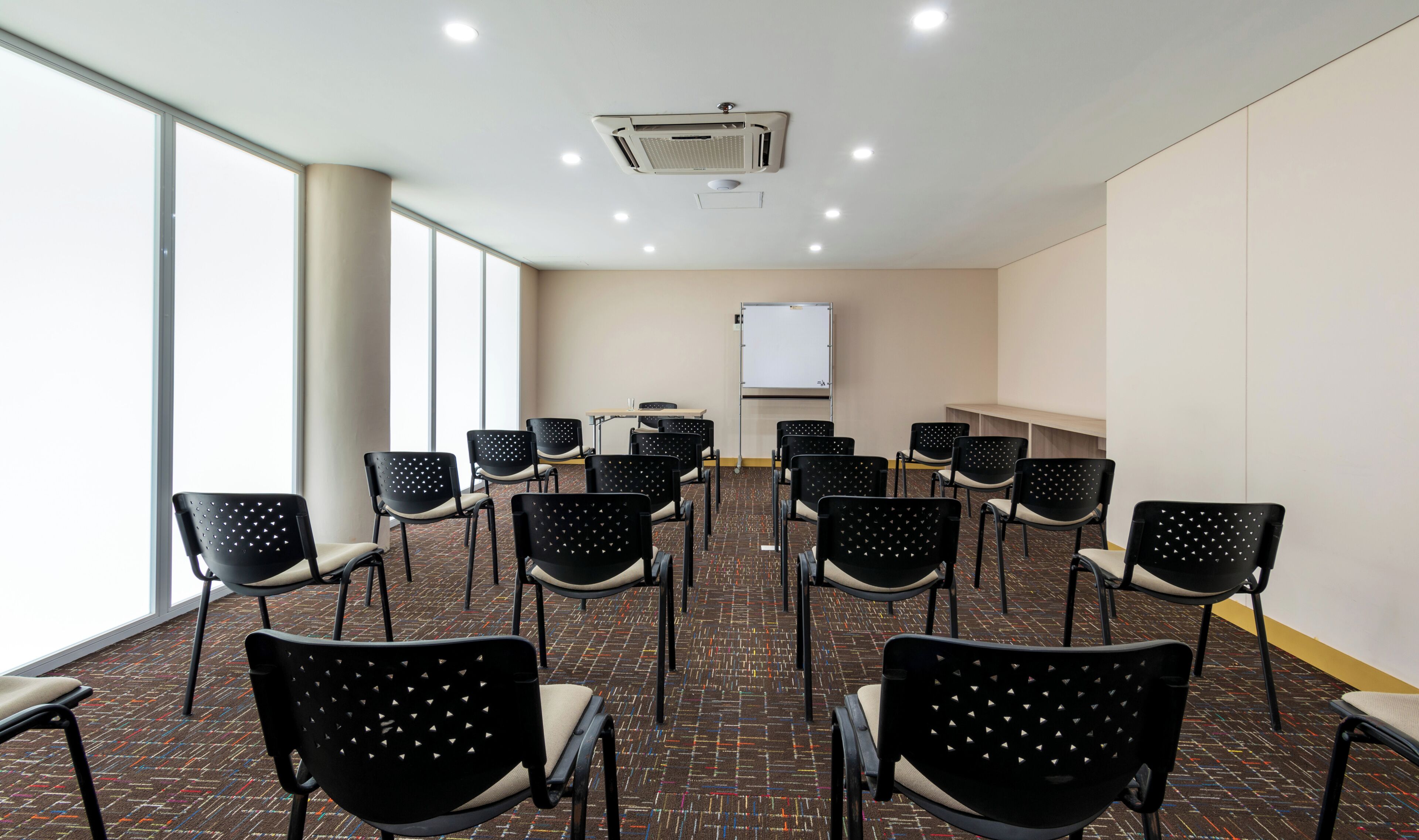 A conference room with rows of chairs, a whiteboard, and a ceiling-mounted air conditioning unit.