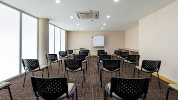 A conference room with rows of chairs, a whiteboard, and a ceiling-mounted air conditioning unit.
