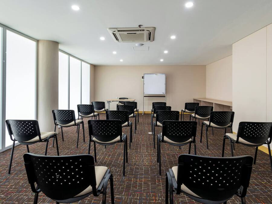 A conference room with rows of chairs, a whiteboard, and a ceiling-mounted air conditioning unit.