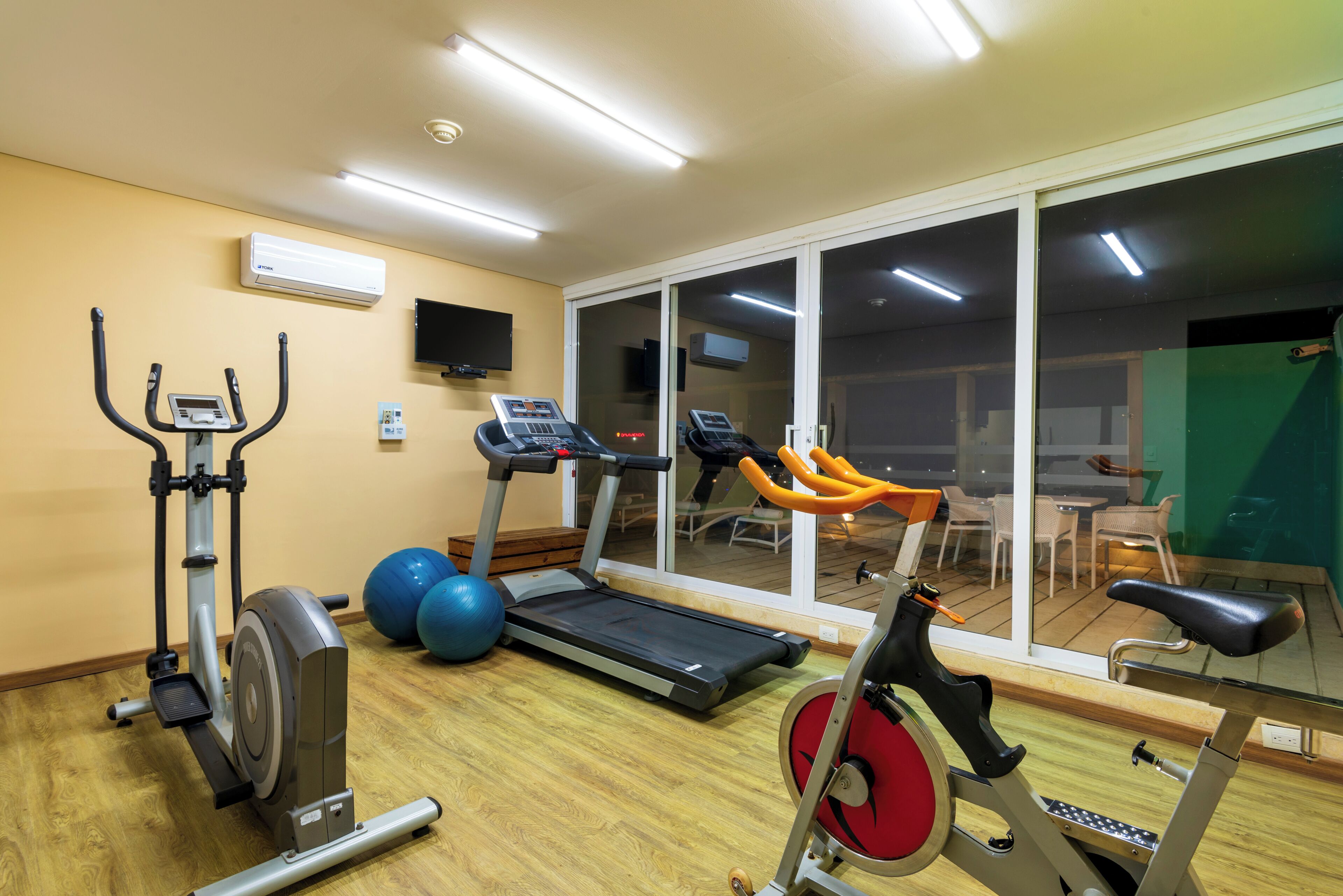 Un gimnasio con equipo de ejercicio, una cinta de correr y un ventanal grande.