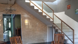 A spacious living area with a high ceiling, a ceiling fan, a staircase, and two wooden chairs. - New Century Hostel (Granada)