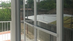 A balcony with large glass doors, a tiled floor, and a view of a residential area with trees and a clear sky. - New Century Hostel (Granada)