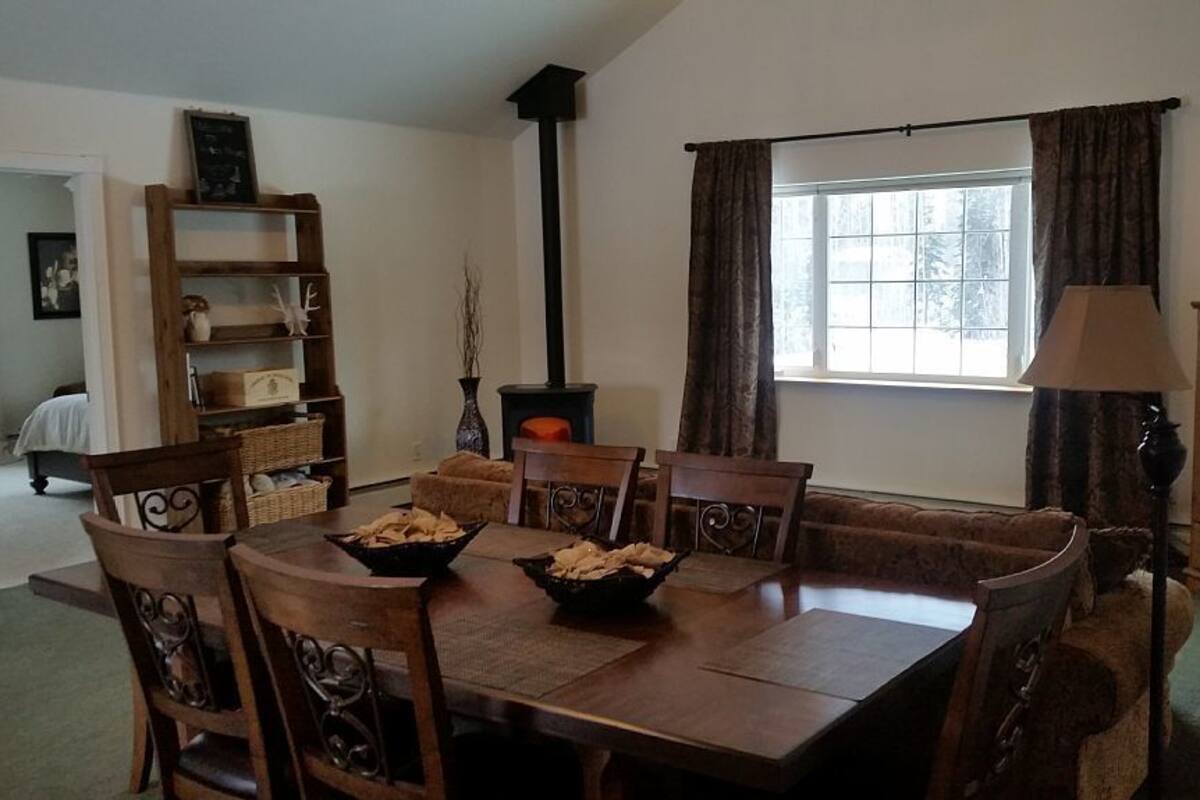 A dining area with a wooden table and chairs, a bookshelf, a fireplace, and a window with curtains.
