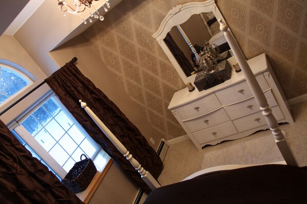 A bedroom with a window, a dresser, and a chandelier.