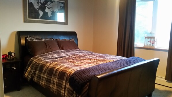 A neatly made bed with a plaid bedspread, a headboard, and a nightstand with a clock.