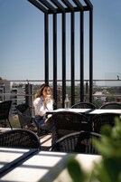 Eine Person sitzt an einem Tisch im Freien und hat einen klaren Blick auf die Stadtlandschaft im Hintergrund.