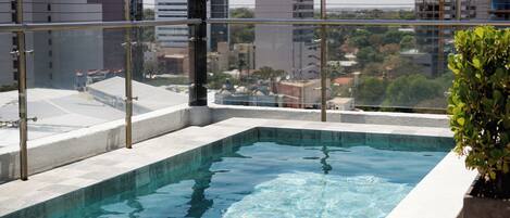 Une piscine sur le toit, avec une eau cristalline, entourée d’une rambarde en verre, et offrant une vue imprenable sur le paysage urbain.