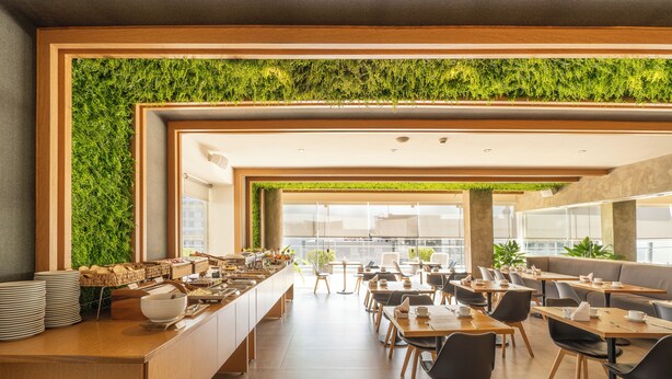 A modern cafe with a long counter, multiple seating areas, and a green wall. - The Hub Urban Hotel (Asunción)