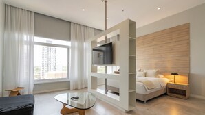 A modern hotel room with a bed, TV, glass table, and a view of the city. - The Hub Urban Hotel (Asunción)
