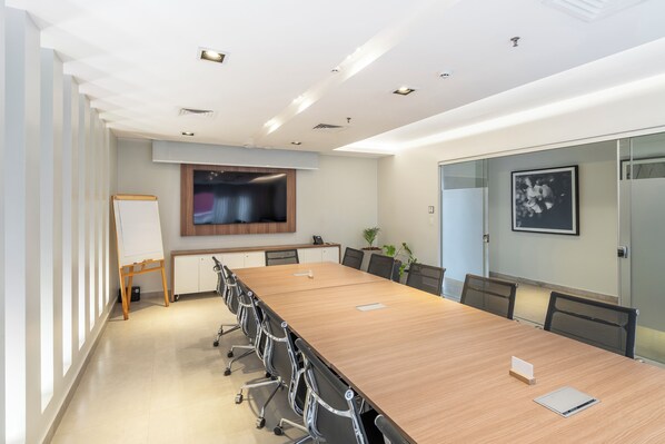 A conference room with a long table, chairs, a whiteboard, and a TV screen. - The Hub Urban Hotel (Asunción)