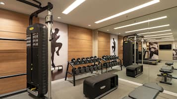 Un gimnasio con equipo de levantamiento de pesas, mancuernas, cintas de correr y un banco.